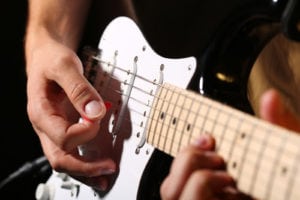Male hands playing electric guitar with plectrum closeup photo. Learning musical instrument music shop or school blues bar or rock cafe having fun enjoying hobby concept