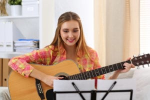 Beautiful smiling woman holding and playing western acoustic guitar portrait. Learning musical instrument music shop or school having fun enjoying hobby concept