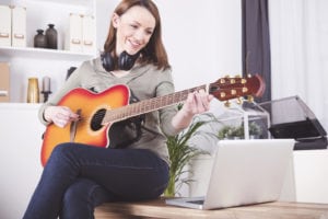 Happy smiling brown haired woman casual dressed playing records on guitar supported by laptop